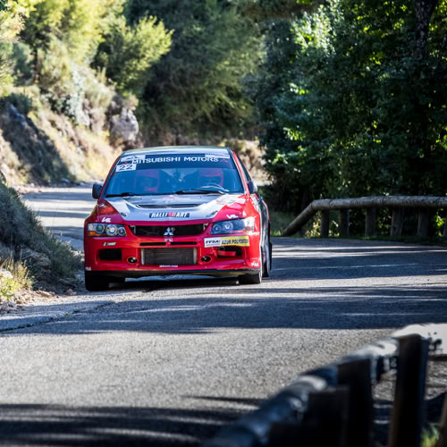 Rallye Une voiture rouge de course sur une route sinueuse entourée d'arbres et de végétation.