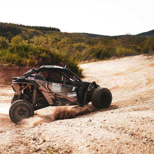 SSV Un véhicule tout-terrain roulant sur un chemin poussiéreux avec des collines et de la végétation en arrière-plan.
